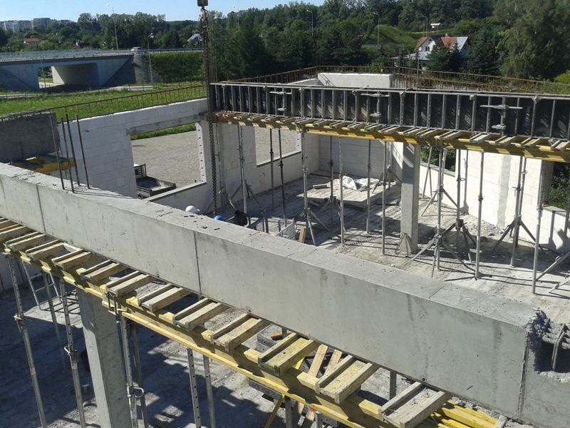 Budynek w trakcie budowy ze ścianami, belkami i szalunkiem betonowym.
