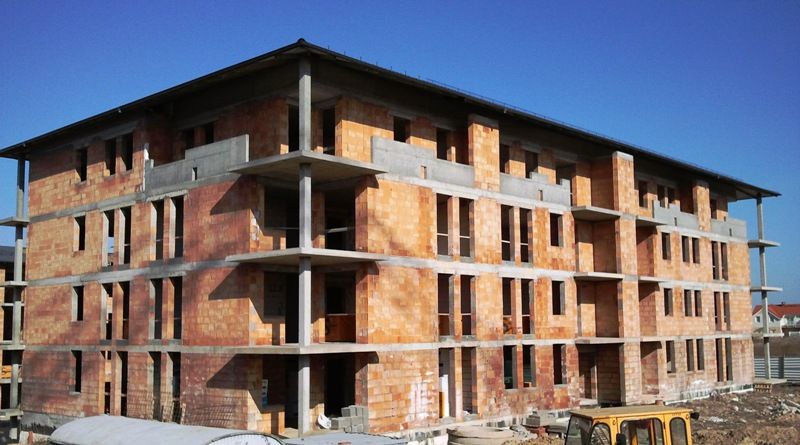 Wielopiętrowy budynek w trakcie budowy z odsłoniętą ceglaną i betonową konstrukcją.