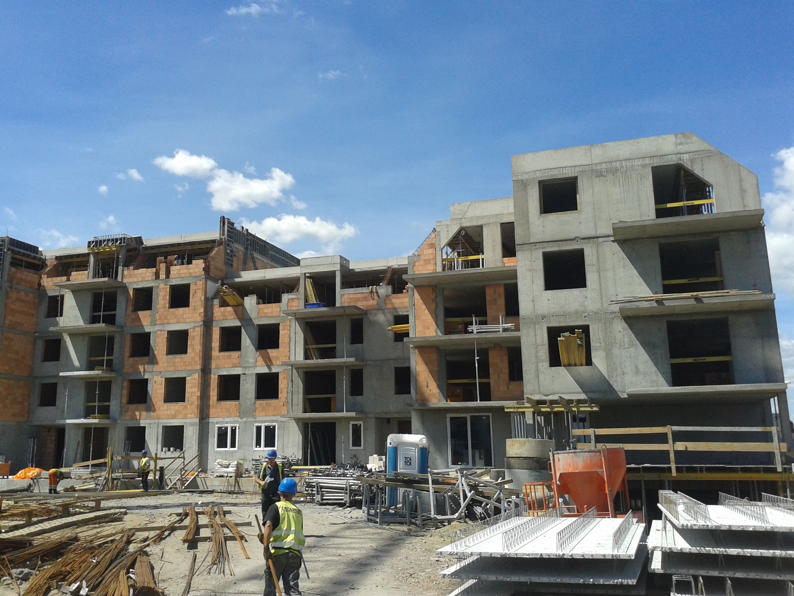 Construction site with multi-story buildings, concrete frames, brickwork, workers, and materials.