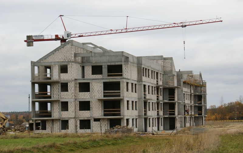 Wielopiętrowy budynek z betonu i bloczków w budowie z użyciem czerwonego dźwigu.