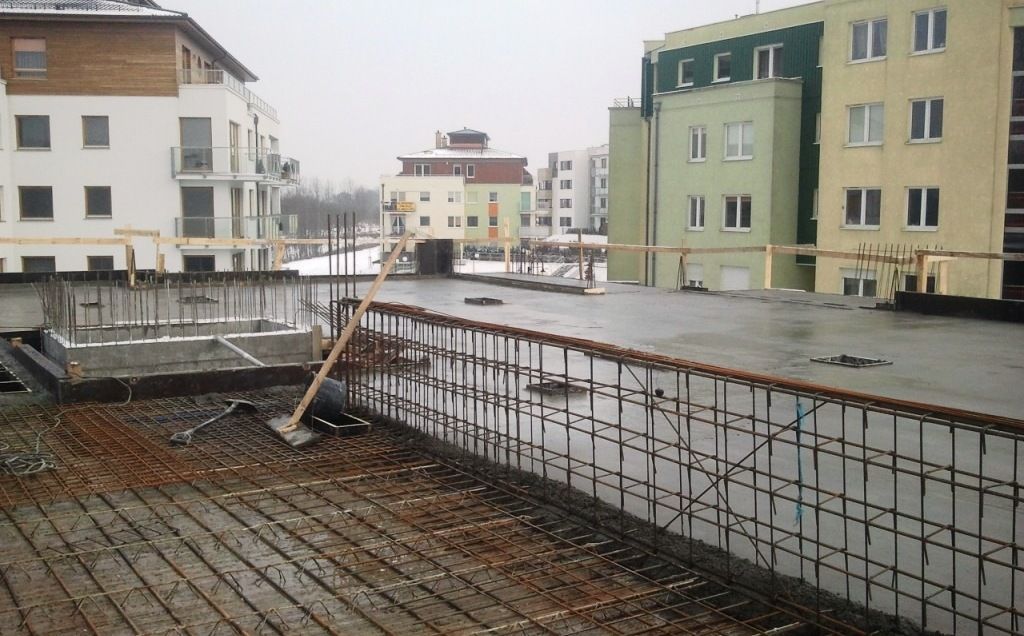 Plac budowy ze zbrojeniem i płytą betonową, otoczony budynkami mieszkalnymi.