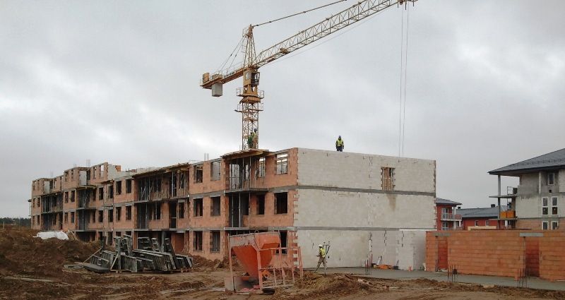 Budowa wielopiętrowego, ceglanego budynku z dużym, żółtym dźwigiem wieżowym i pracownikami na placu budowy.