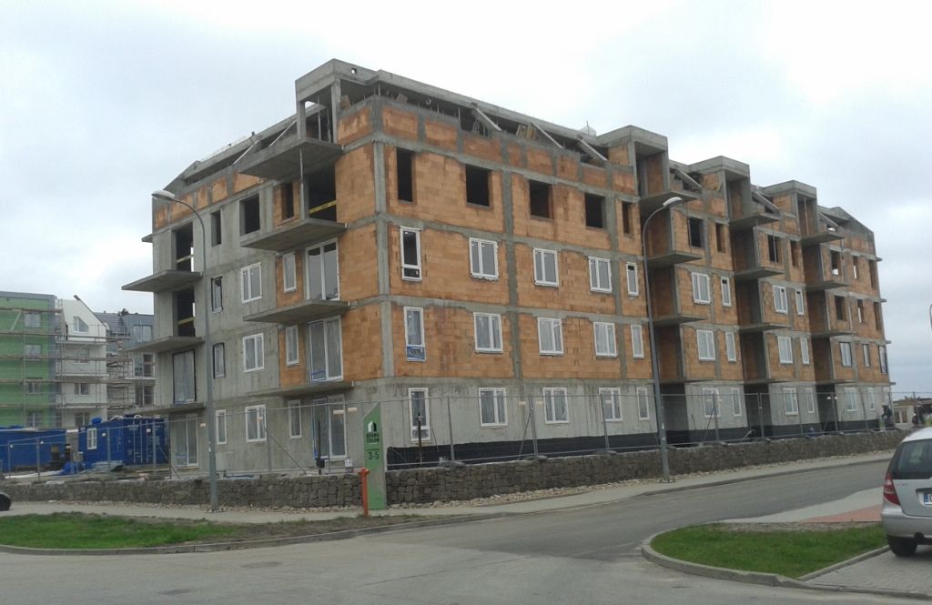 Wielopiętrowy budynek mieszkalny w trakcie budowy z odsłoniętą cegłą, betonem i białymi oknami.