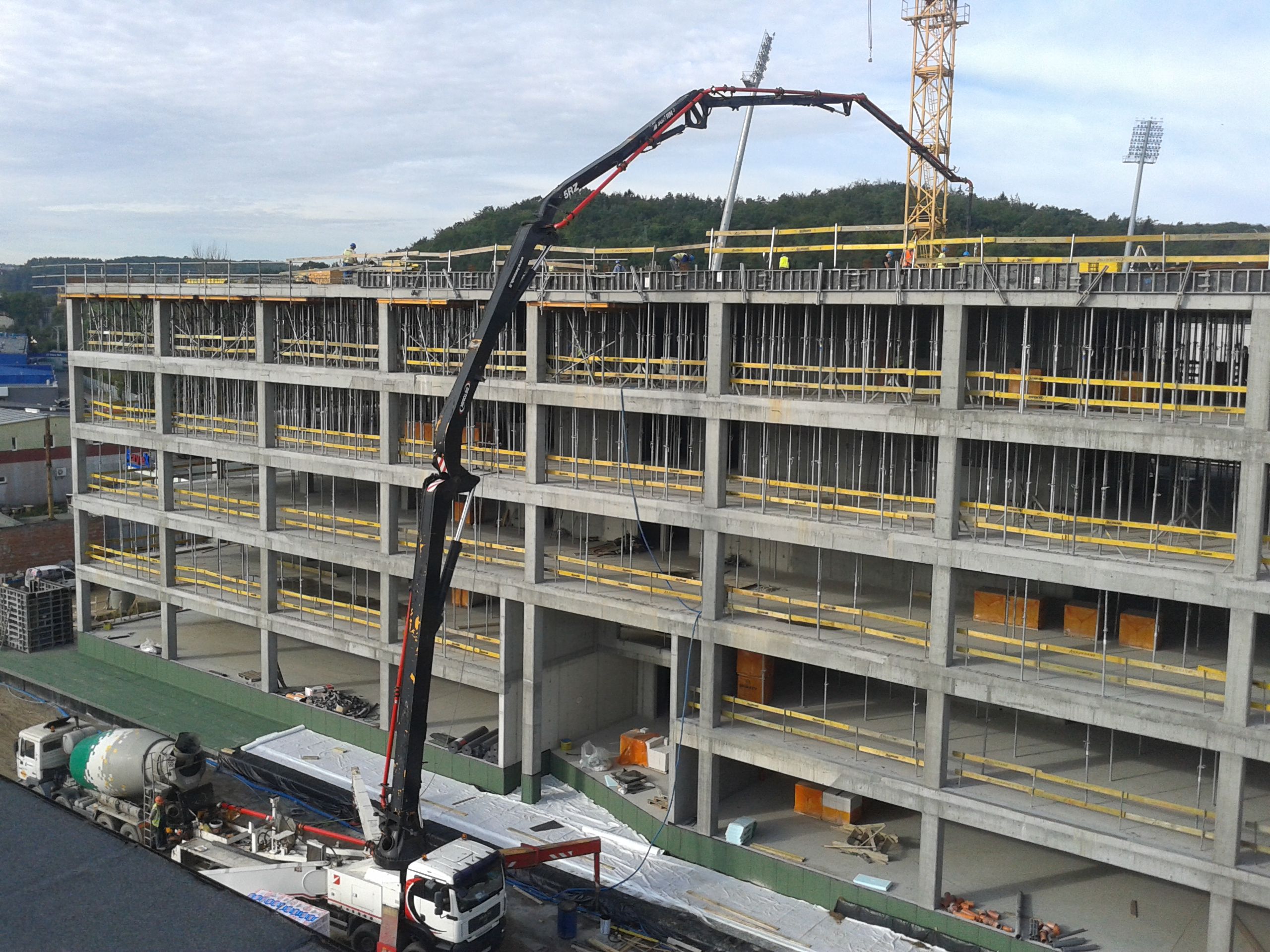 A large concrete pump truck pours concrete into the upper floors of a multi-story building under construction.