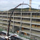 A large concrete pump truck pours concrete into the upper floors of a multi-story building under construction.