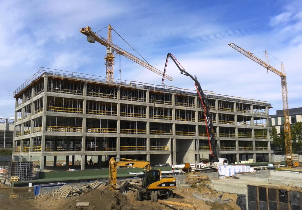 A large concrete pump truck pours concrete into the upper floors of a multi-story building under construction.