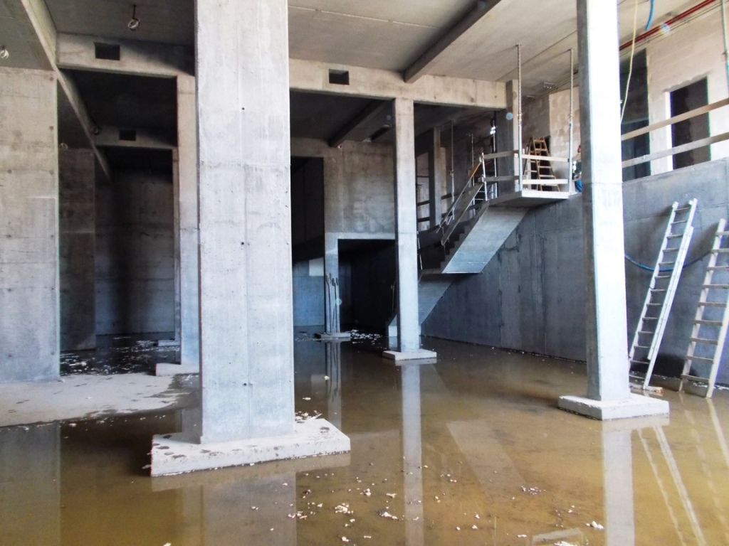 Zalany betonowy budynek w trakcie budowy z filarami, schodami i drabinami.