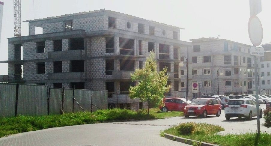 Budynki wielopiętrowe w budowie z odsłoniętymi ścianami z bloczków, dźwigiem i parkingiem dla samochodów.