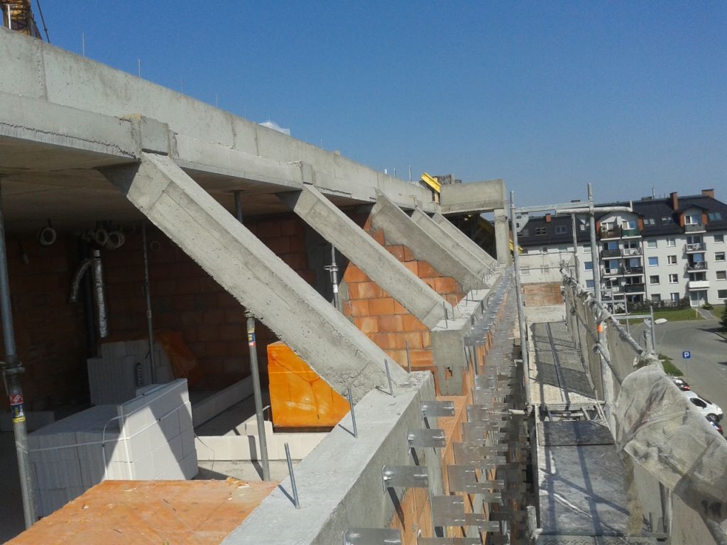 Plac budowy z betonowymi belkami, odsłoniętymi ścianami z cegły i rusztowaniami.