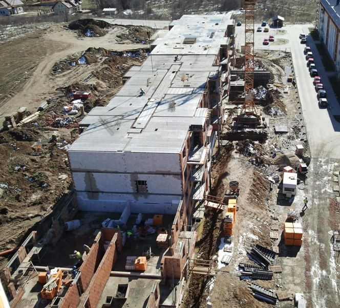 Widok z lotu ptaka na wielopiętrowy budynek w budowie, z dźwigiem i pracownikami.