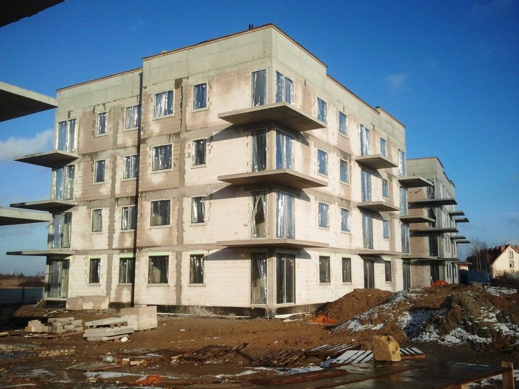 Niedokończony, wielopiętrowy budynek z betonowymi płytami balkonowymi na ziemnym placu budowy.