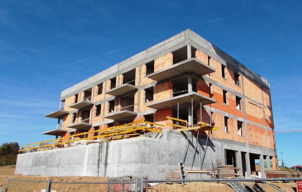 Budynek wielopiętrowy w trakcie budowy z odsłoniętymi ścianami betonowymi i ceglanymi.