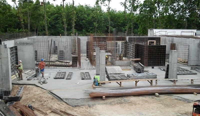 Budowa fundamentów i ścian w trakcie budowy, zbrojenie, szalunki i pracownicy.