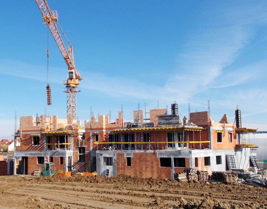 Wielopiętrowy budynek w budowie z odsłoniętą cegłą i dużym żółtym dźwigiem wieżowym.