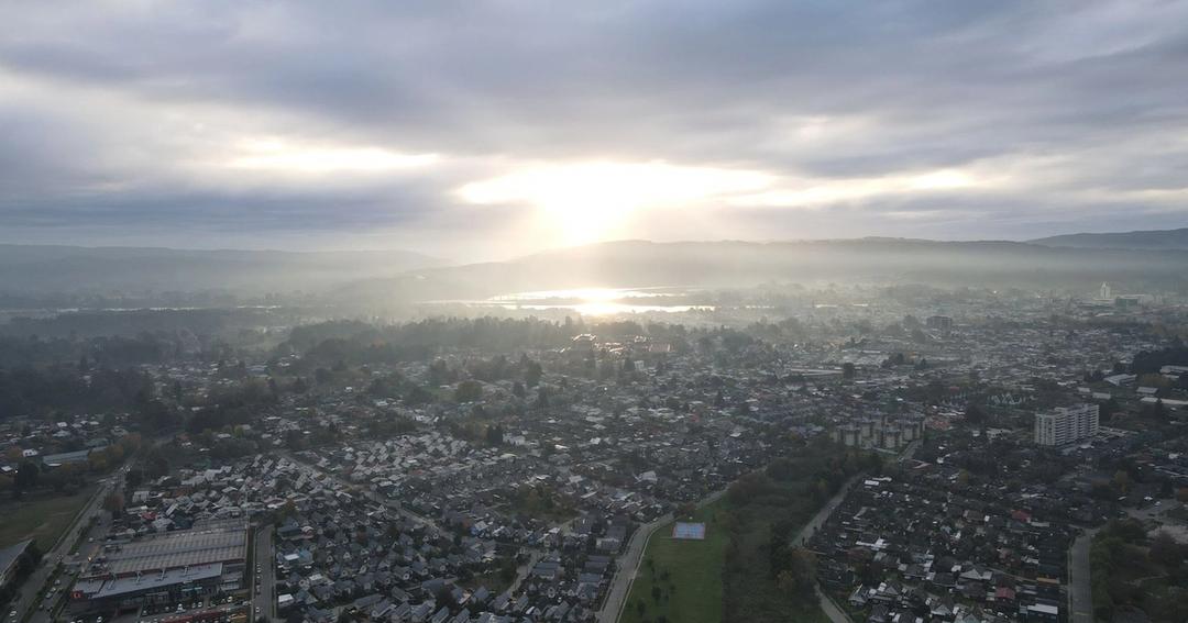 Imagen referencial: Vista aérea de Valdivia al amanecer, que muestra un horizonte brumoso y un cielo nublado iluminado por la salida del sol.