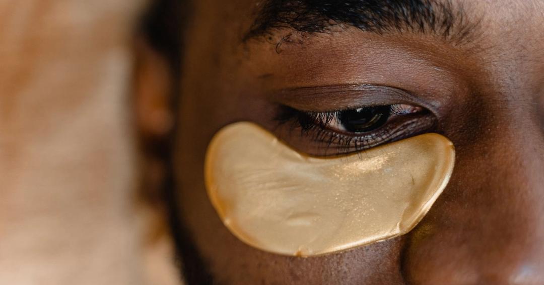 Imagen referencial: Primer plano del ojo de un hombre con un parche dorado bajo los ojos, enfocado en el cuidado de la piel y la rejuvenecimiento.