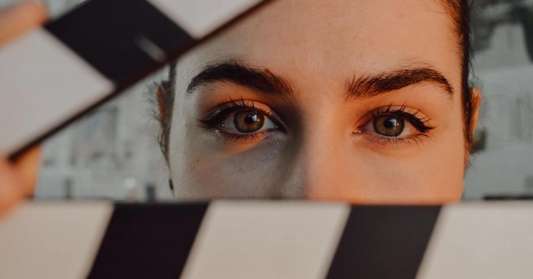 Imagen referencial: Primer plano intrigante de los ojos de una persona detrás de una pizarra de cine, simbolizando la creatividad en la realización de películas.