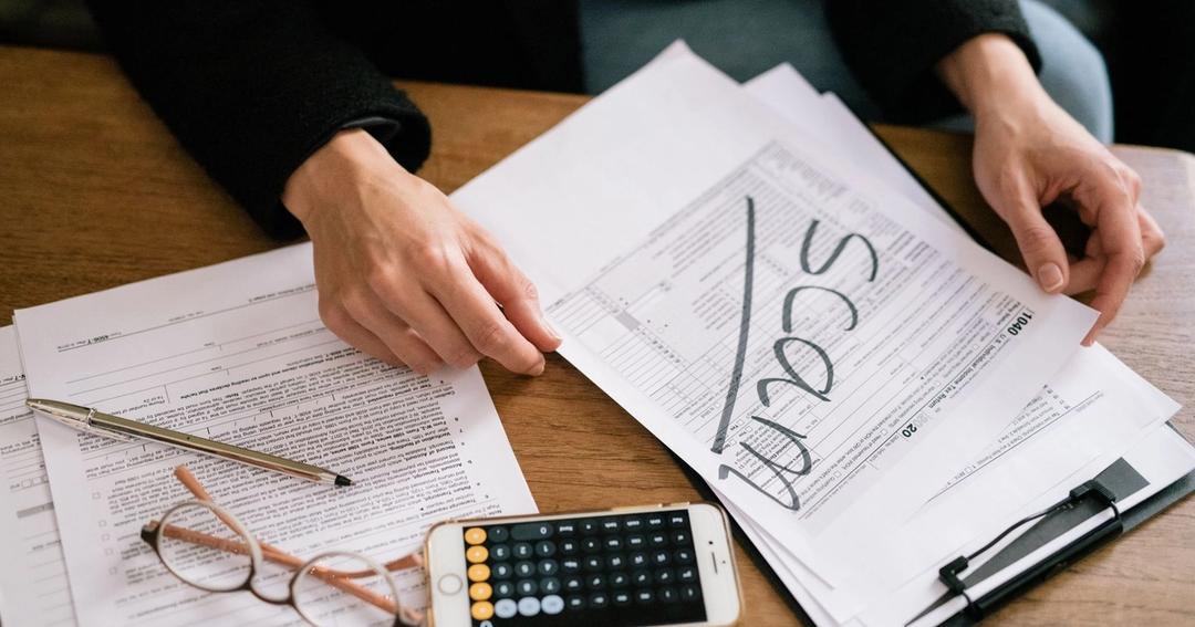 Imagen referencial: Manos de una persona examinando formularios de impuestos etiquetados como estafa, con calculadora y papeles.