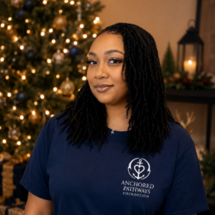The founder of Anchored Pathways Foundation wearing the foundation shirt, beside a warmly lit Christmas tree
