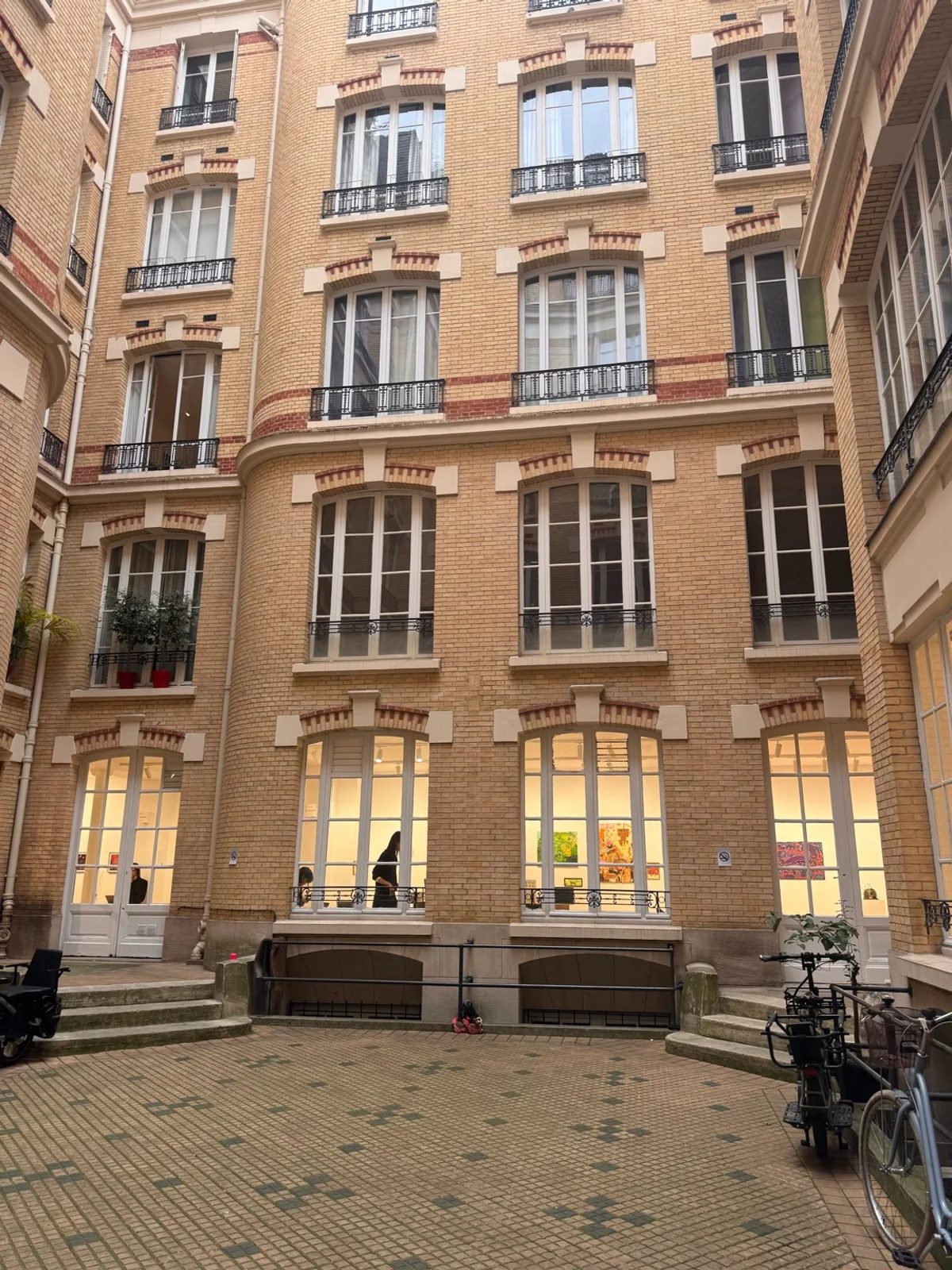 The Post-Fair Paris 2026 courtyard, with illuminated gallery windows, artworks and bicycles.