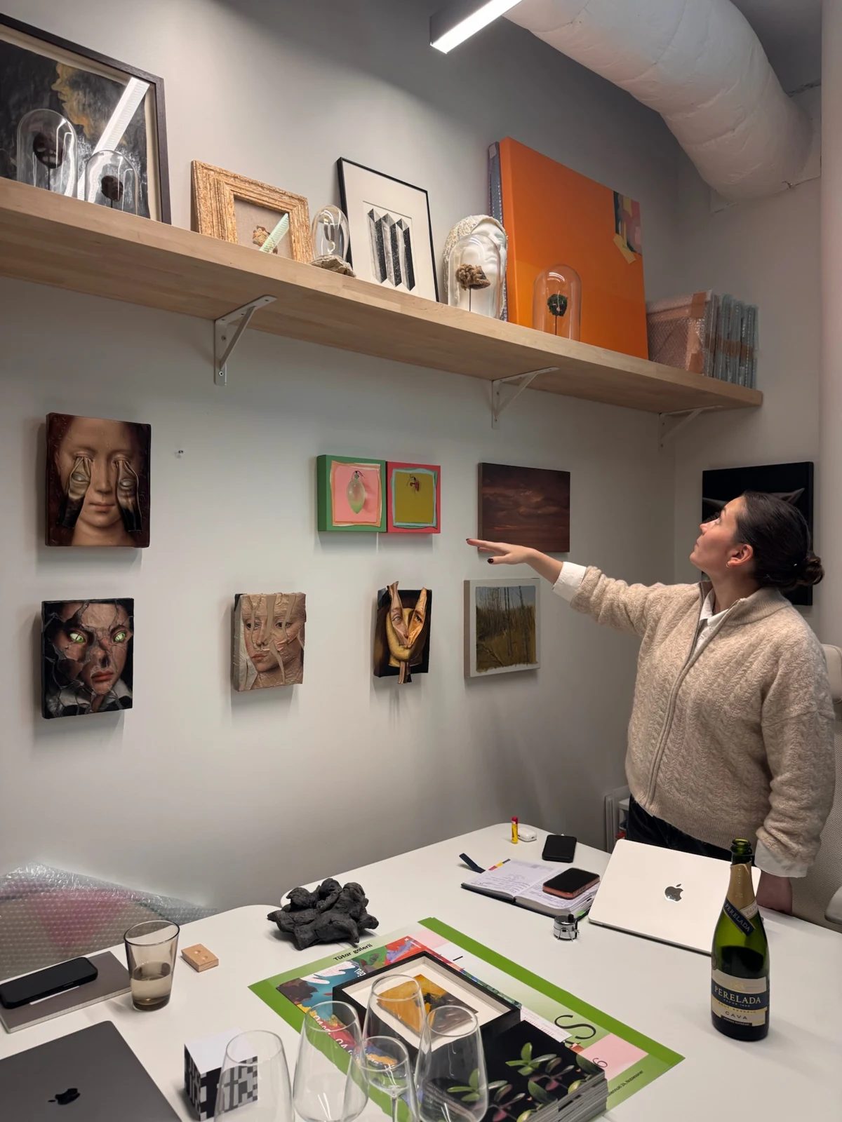 A gallery representative gestures towards artworks displayed on a wall and shelf.