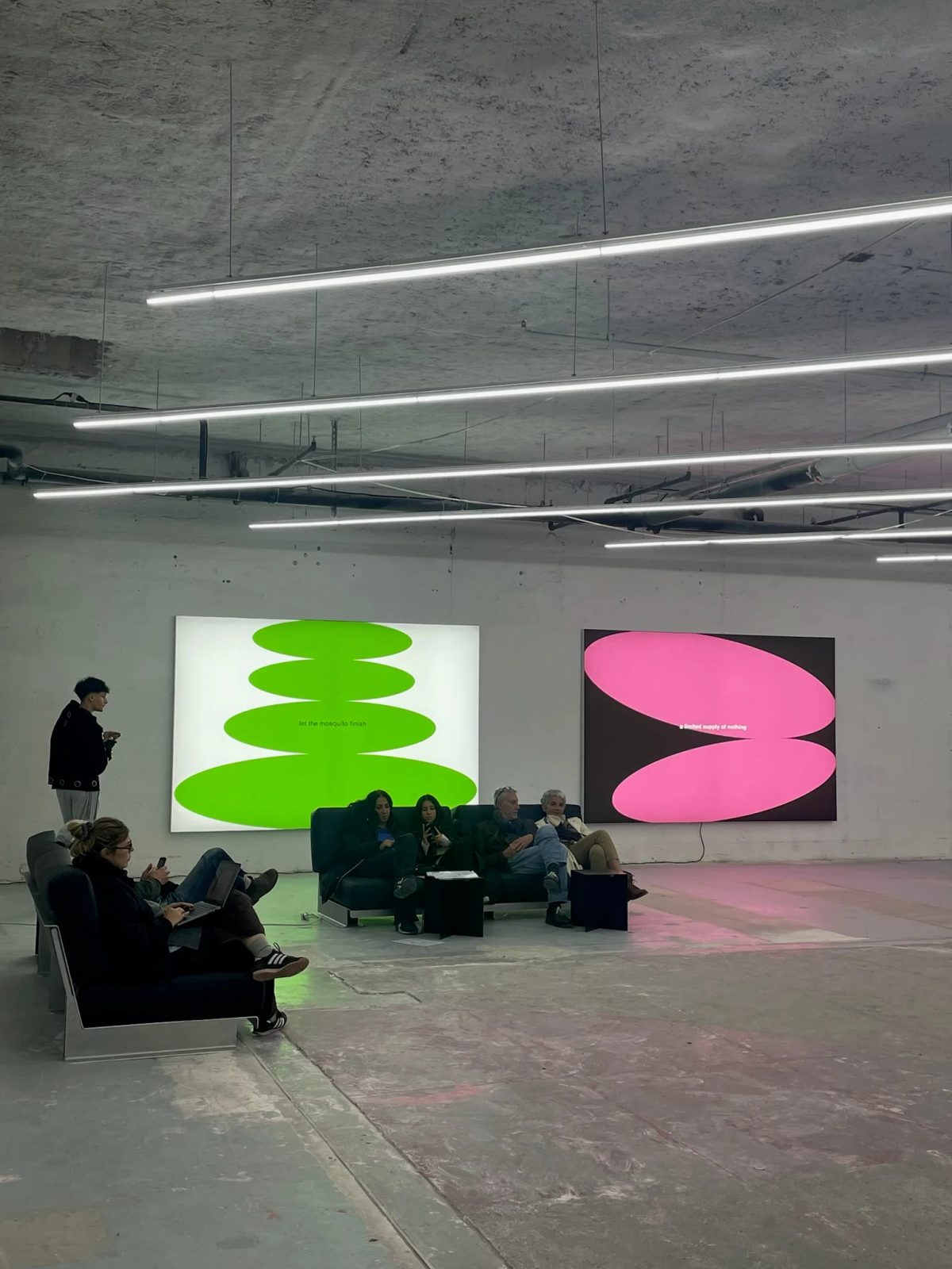 Visitors seated beneath strip lighting beside bright green and pink artworks at Paris Internationale.