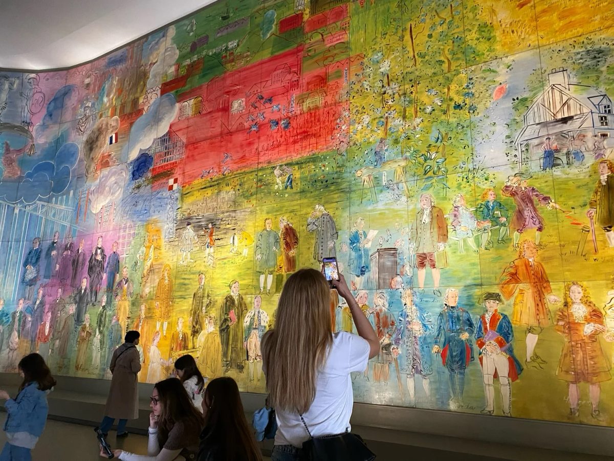 Visitors viewing a colourful wall-sized mural with painted figures and city scenes.