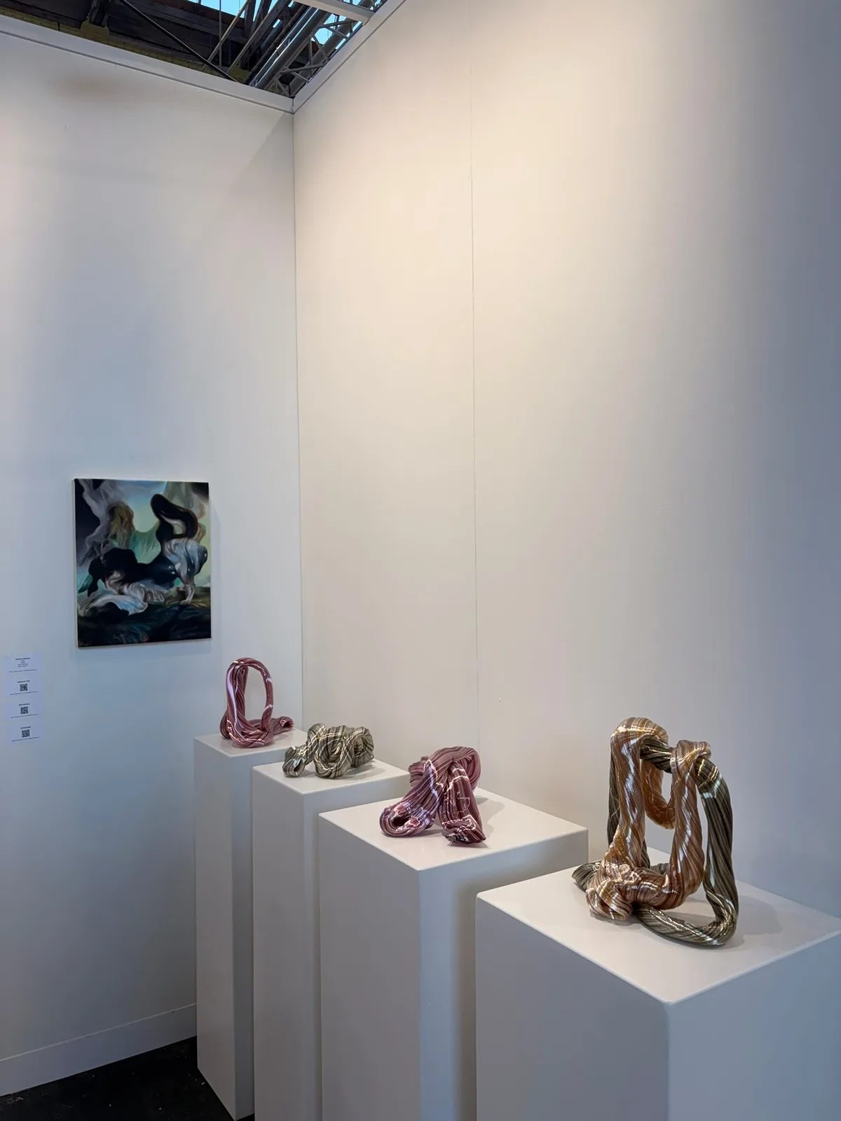 Twisting pink, green and amber glass sculptures displayed on white plinths.