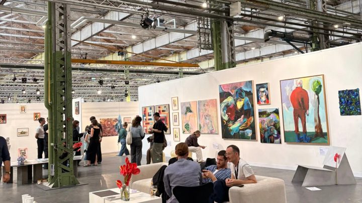 Visitors talking beside colourful paintings at Enter Art Fair inside a former locomotive hall.
