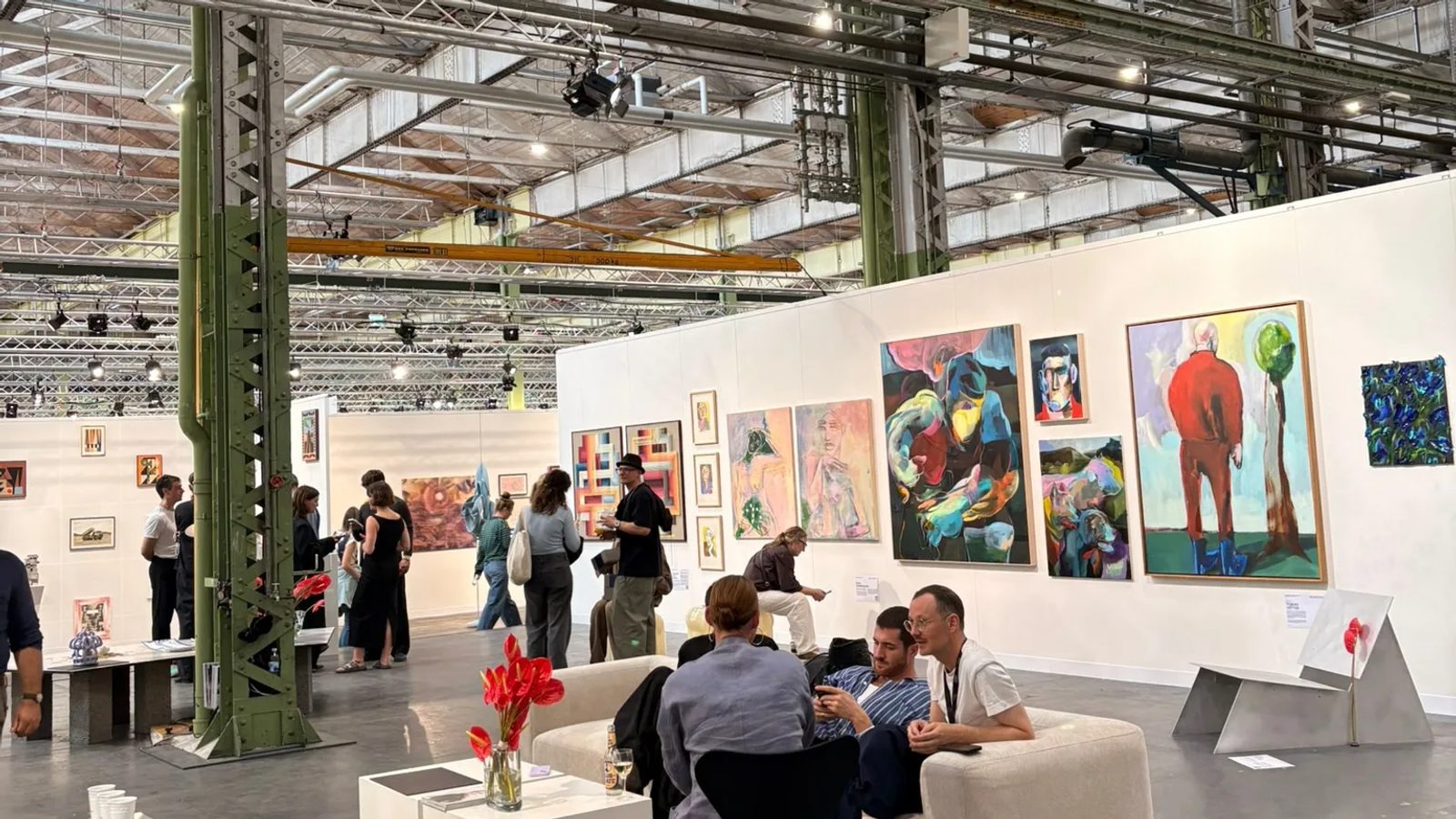 Visitors talking beside colourful paintings at Enter Art Fair inside a former locomotive hall.