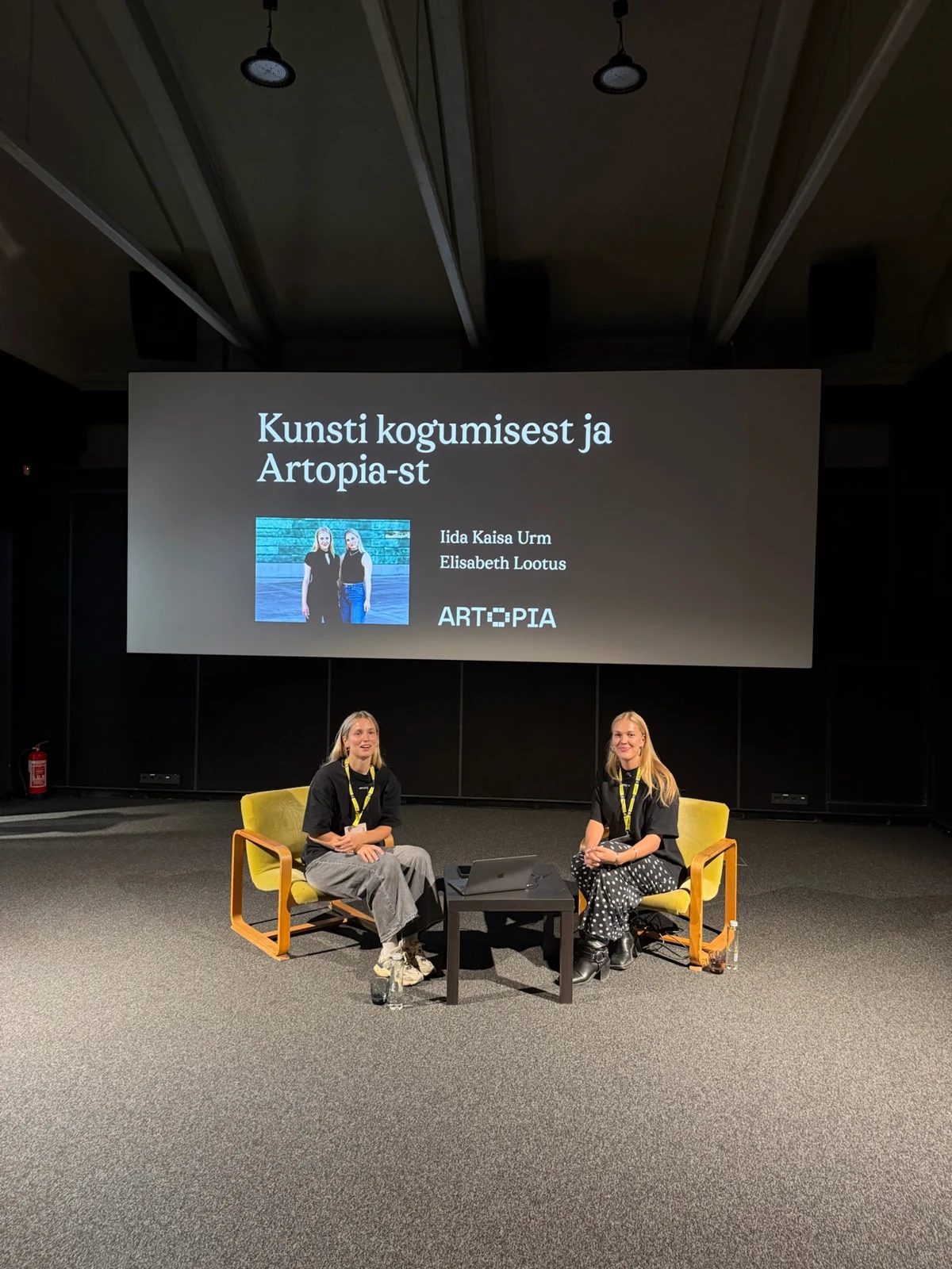 Two speakers seated beneath a screen introducing Artopia at FOTO Tallinn.