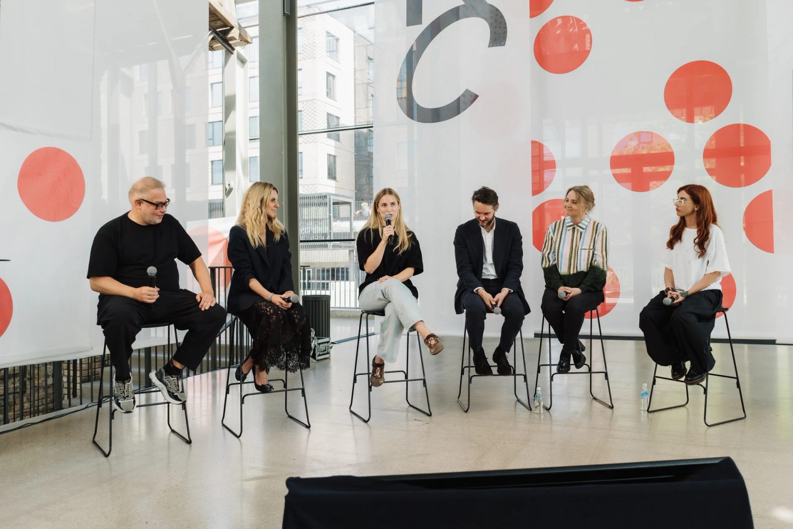 Six panellists seated on stage at Riga Contemporary, with a speaker holding a microphone.