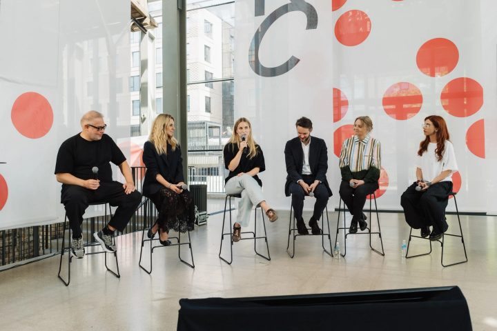 Six panellists seated on stage at Riga Contemporary, with a speaker holding a microphone.