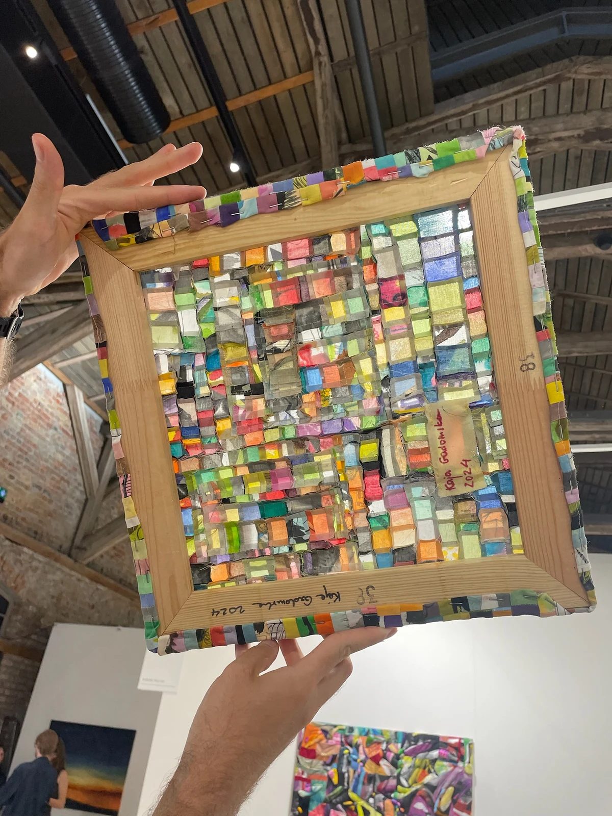 The reverse of a Kaja Gadomska textile work held up to reveal colourful patchwork stretched over a wooden frame.