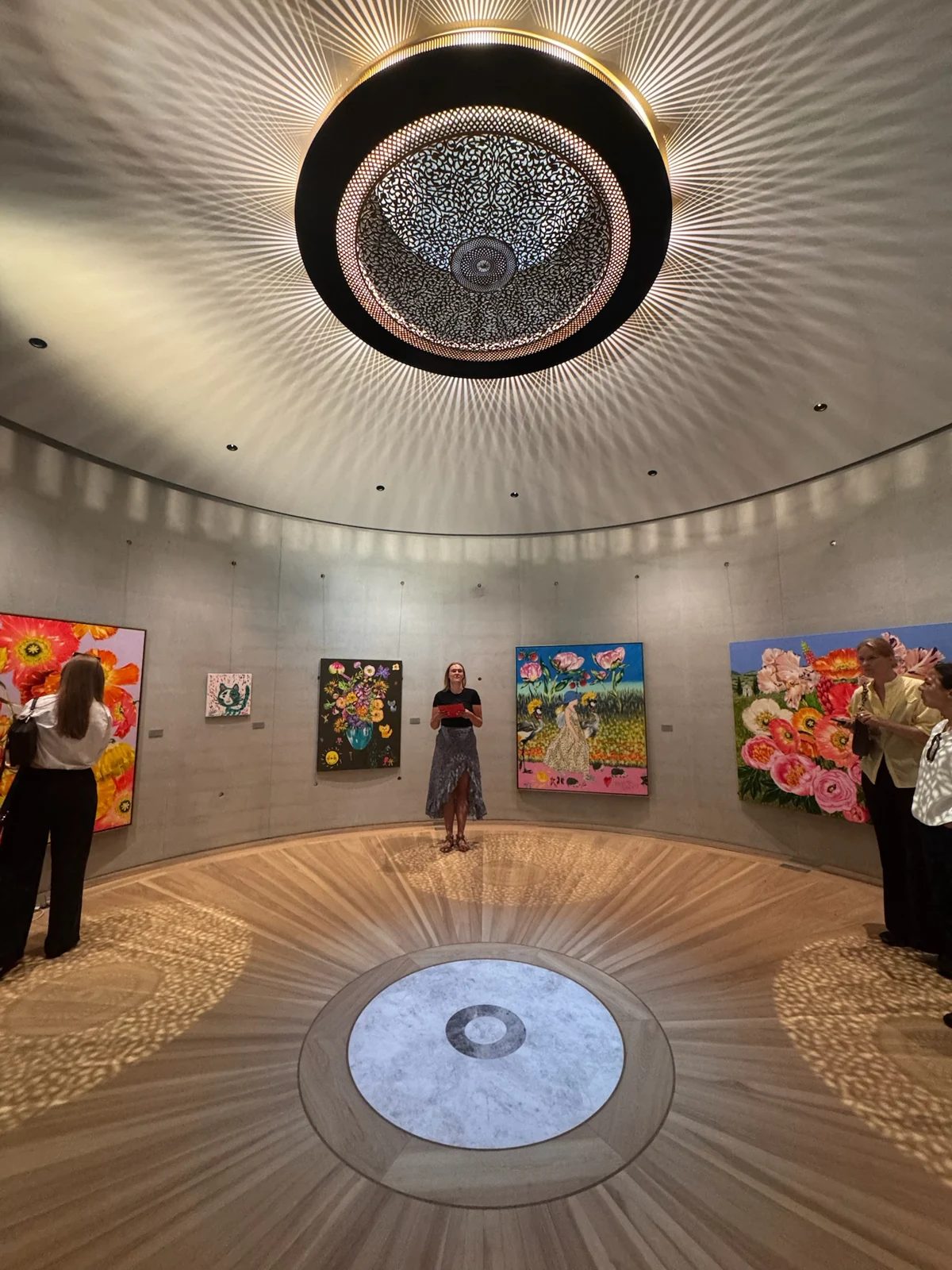 Visitors and colourful paintings in Ola Foundation’s circular gallery, beneath a light casting patterned shadows.
