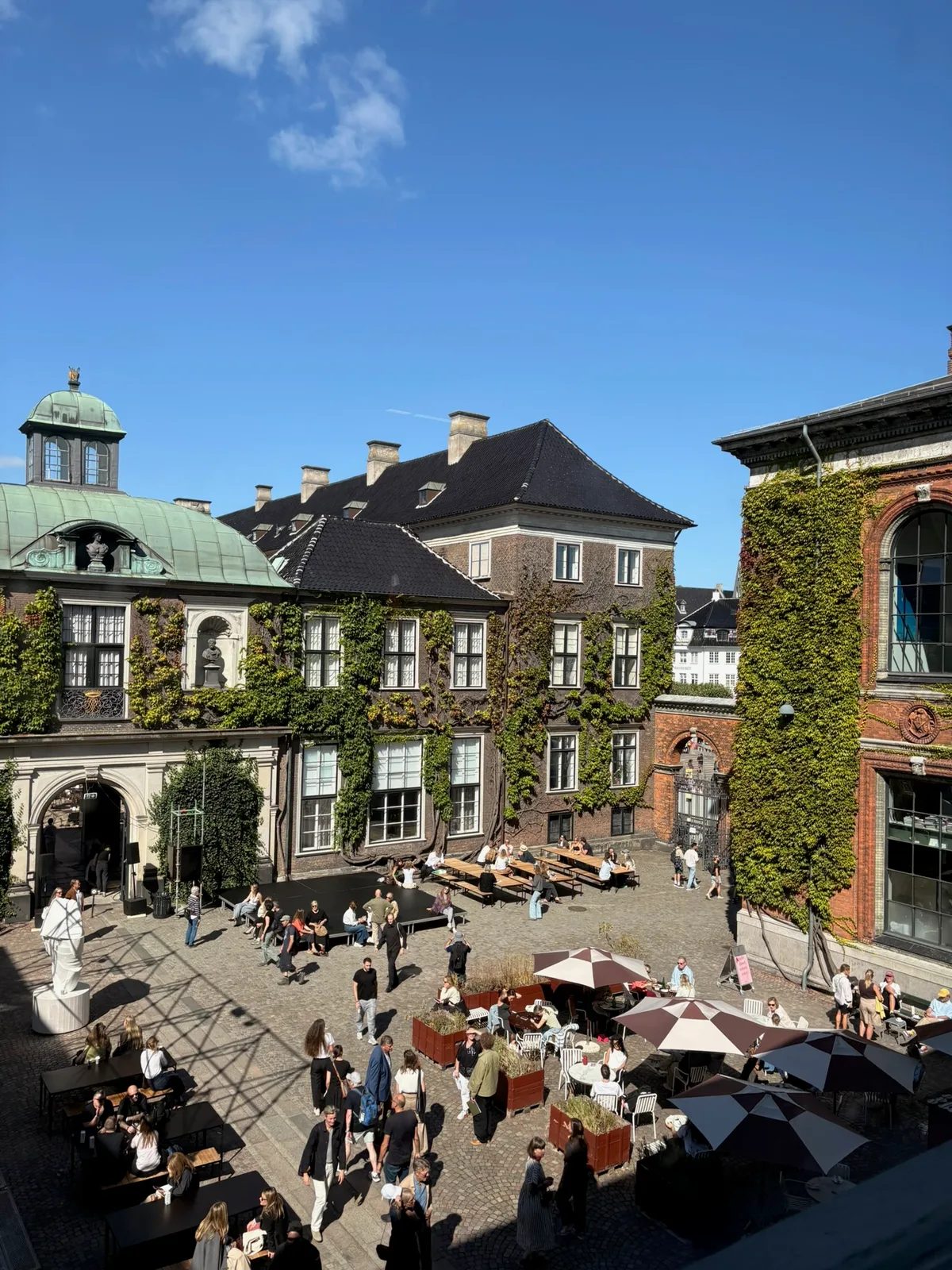 Visitors in the cobbled courtyard of Kunsthal Charlottenborg, surrounded by ivy-covered buildings.