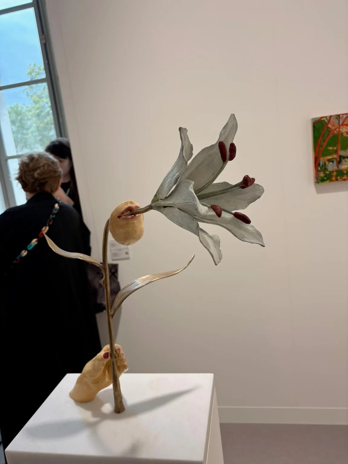 A ceramic hand holds a lily whose stem emerges from a sculpted mouth, by Paloma Proudfoot.