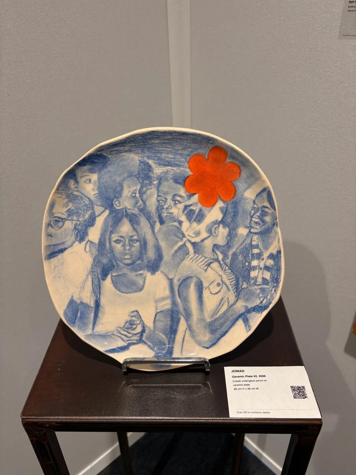 Jomad’s Ceramic Plate #2 (2026), with blue group portraits and an orange flower, shown by OOA Gallery at AKAA.