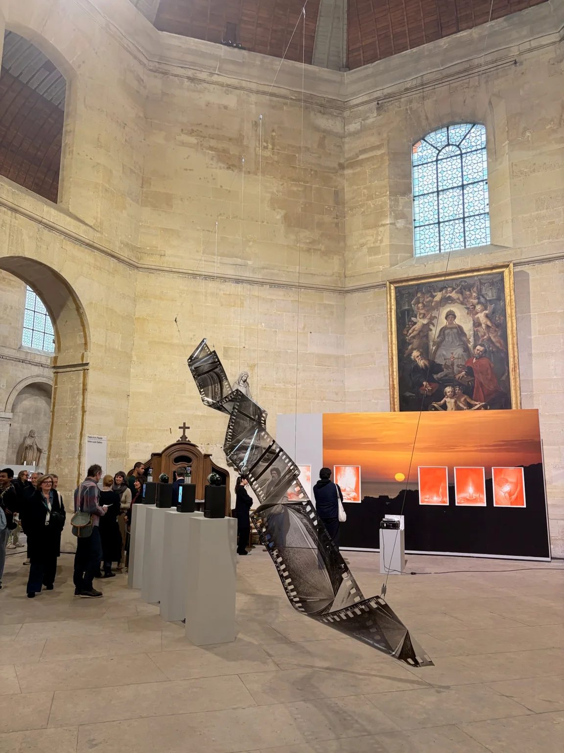 Visitors and a suspended film-strip sculpture inside the Chapelle Saint-Louis de la Salpêtrière at OFFSCREEN Paris.