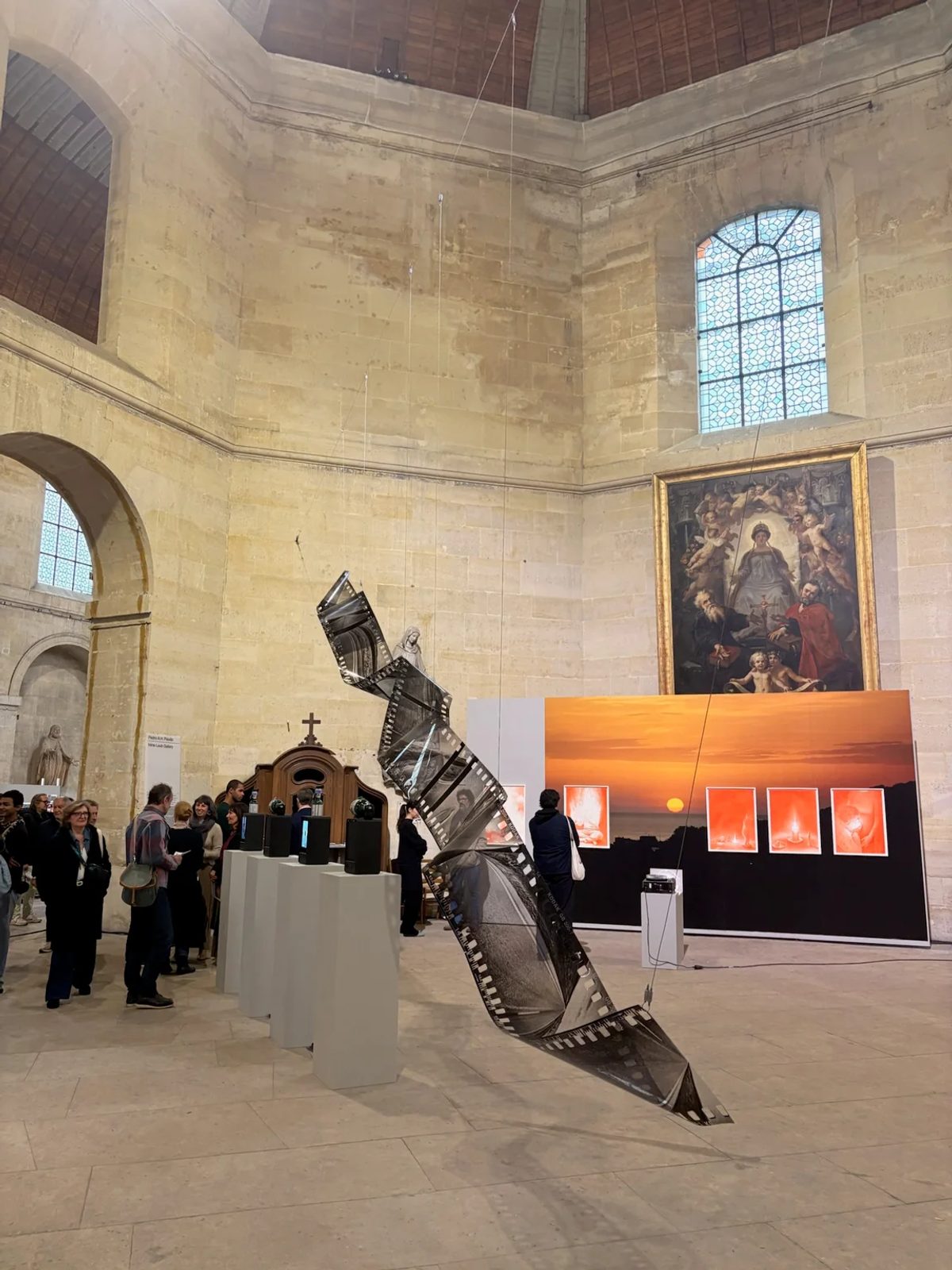 Visitors and a suspended film-strip sculpture inside the Chapelle Saint-Louis de la Salpêtrière at OFFSCREEN Paris.