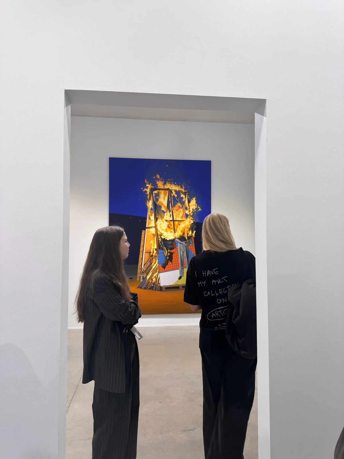 Two visitors viewing a colourful painting through an open gallery doorway.