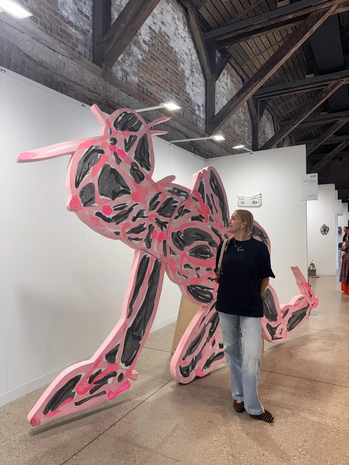 A visitor beside a large pink-and-black animal-shaped sculpture inside an art fair exhibition.