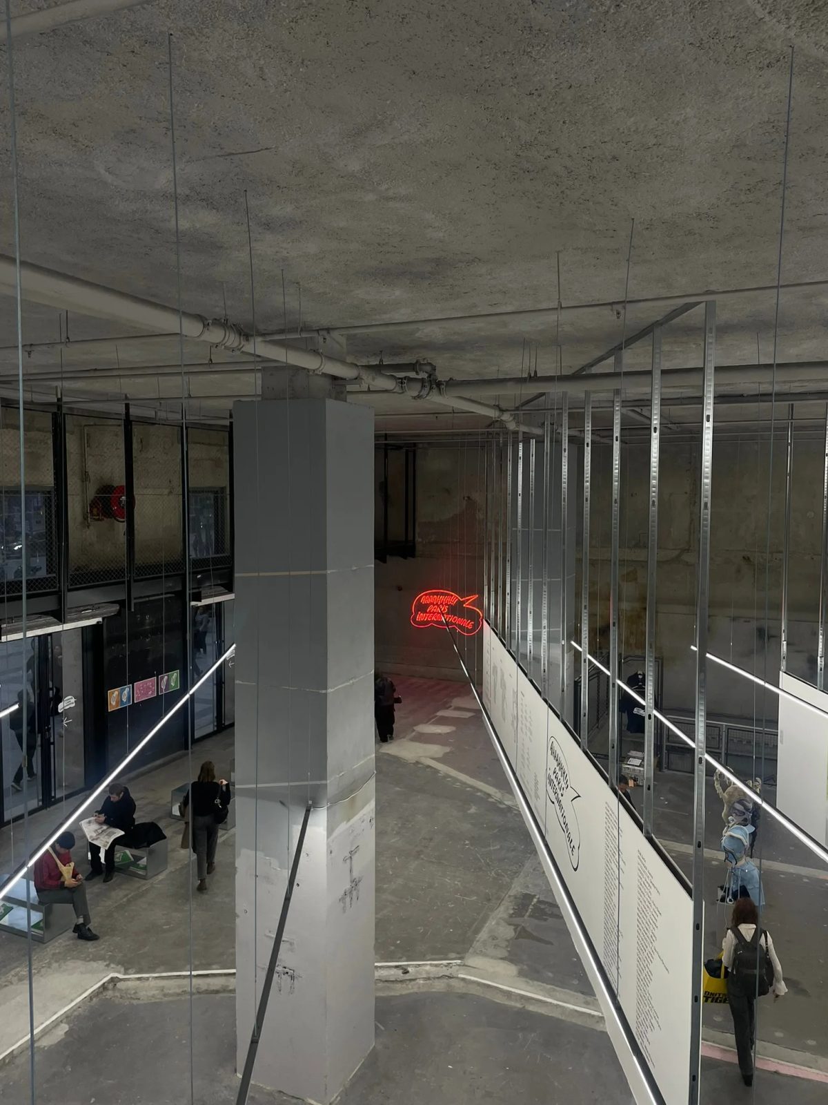 Visitors and exhibition partitions inside an industrial space at Paris Internationale, with a red neon sign.
