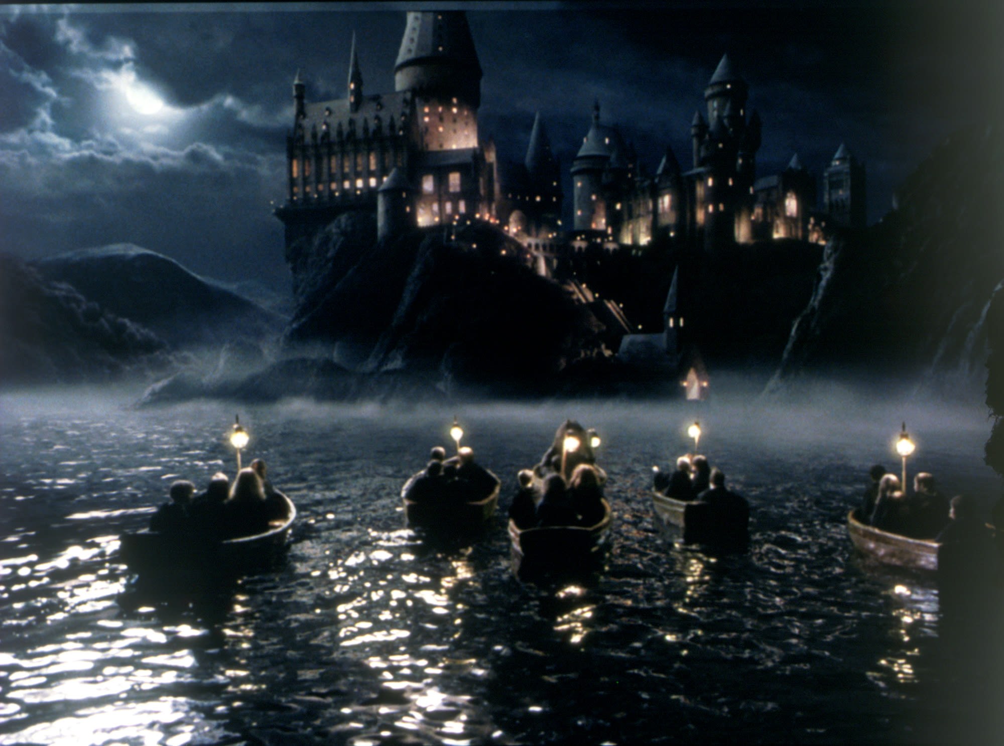 First-year Hogwarts students cross the lake in small boats at night.