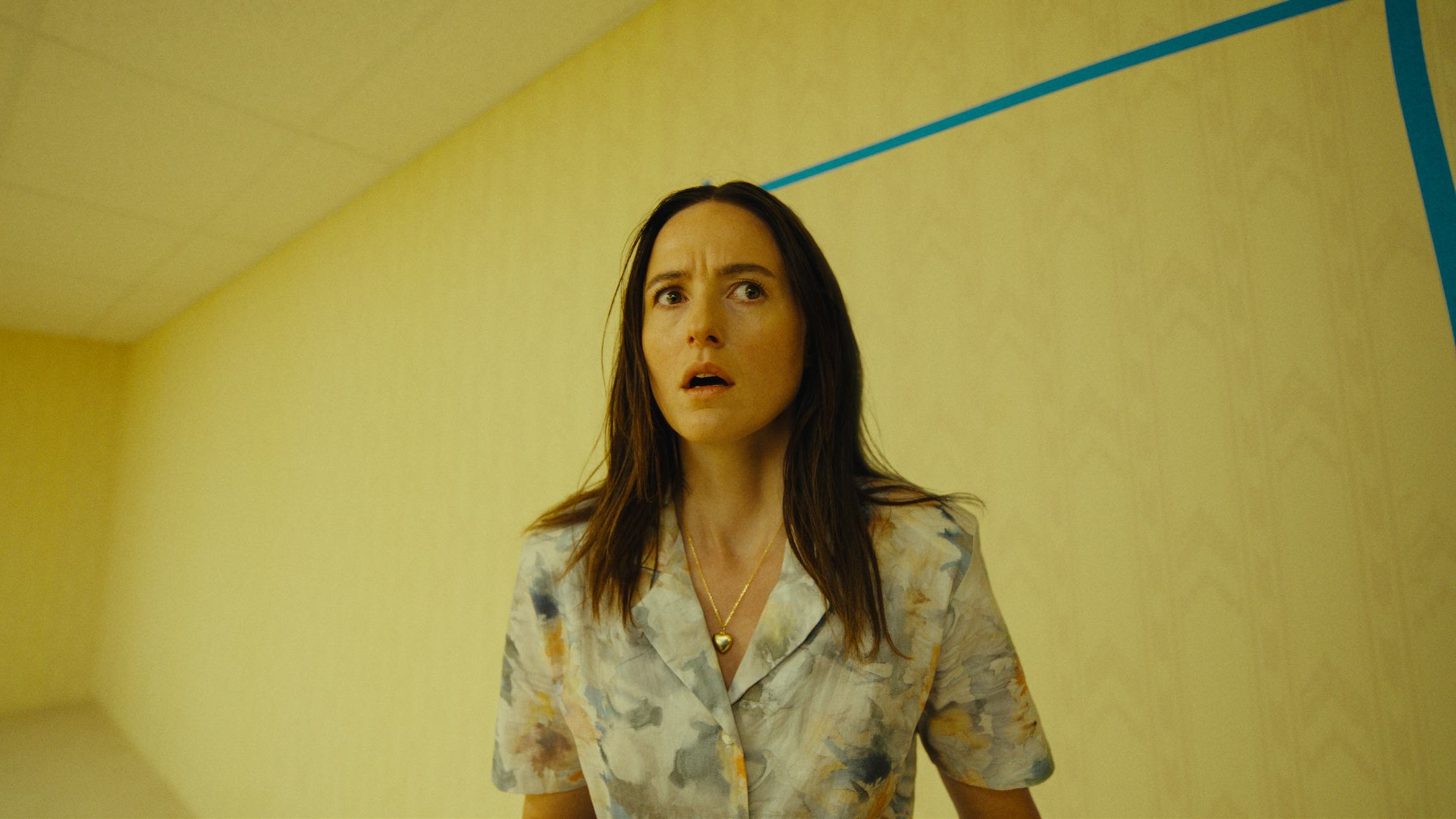 Renate Reinsve stands in an empty yellow Backrooms hallway in A24's Backrooms trailer image.