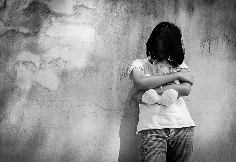 Jente står foran en vegg og holder en bamse (colourbox.com)