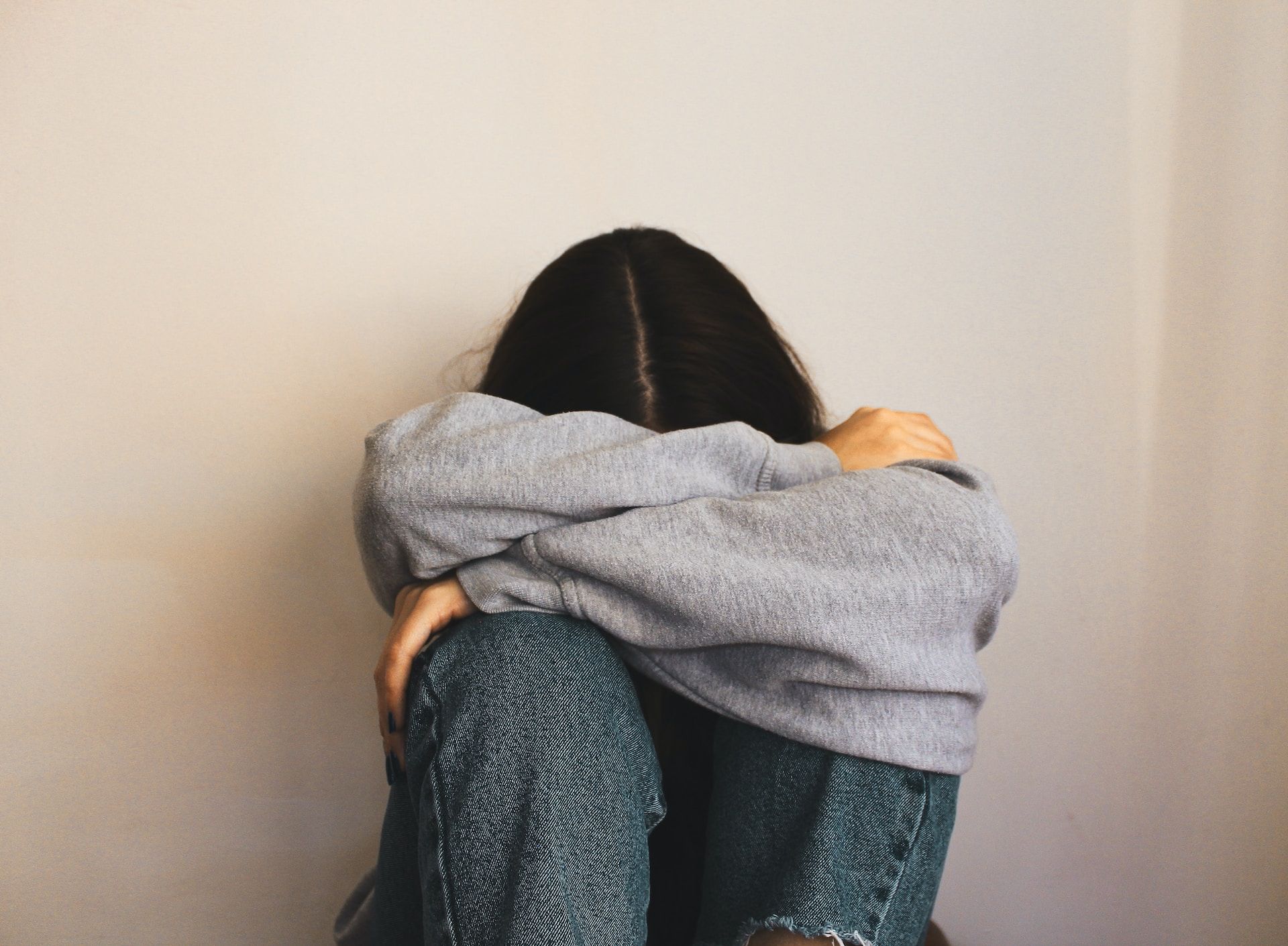Foto av en ung person som ser lei seg ut. Personen sitter inntil en vegg og holder rundt seg selv.