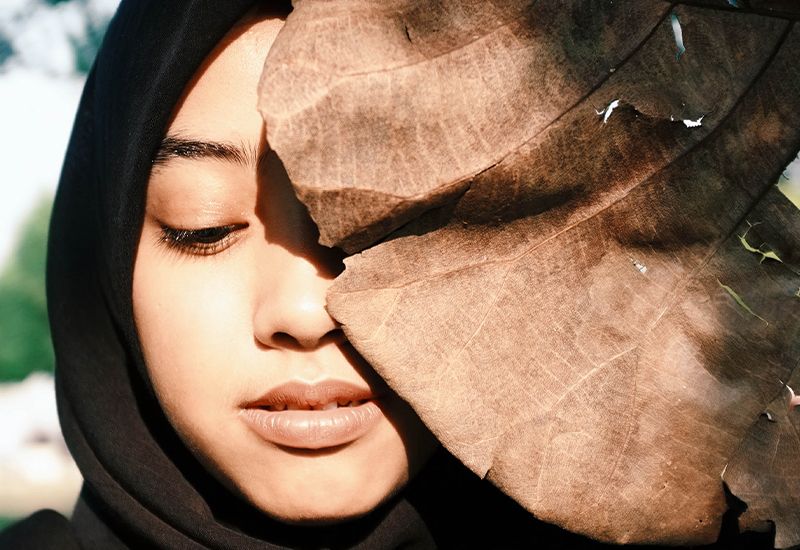 Jente med hijab som har ansiktet delvis gjemt bak et blad. 