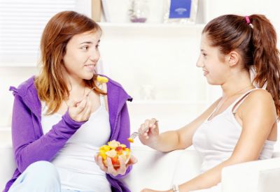 To tenåringsjenter sitter med en skål med frukt foran seg og spiser. (www.colourbox.com)