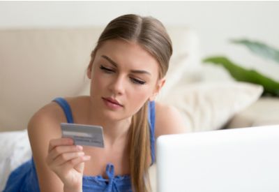 En tenåringsjente sitter foran en datamaskin og ser på kredittkortet hun holder foran seg. (www.colourbox.com)